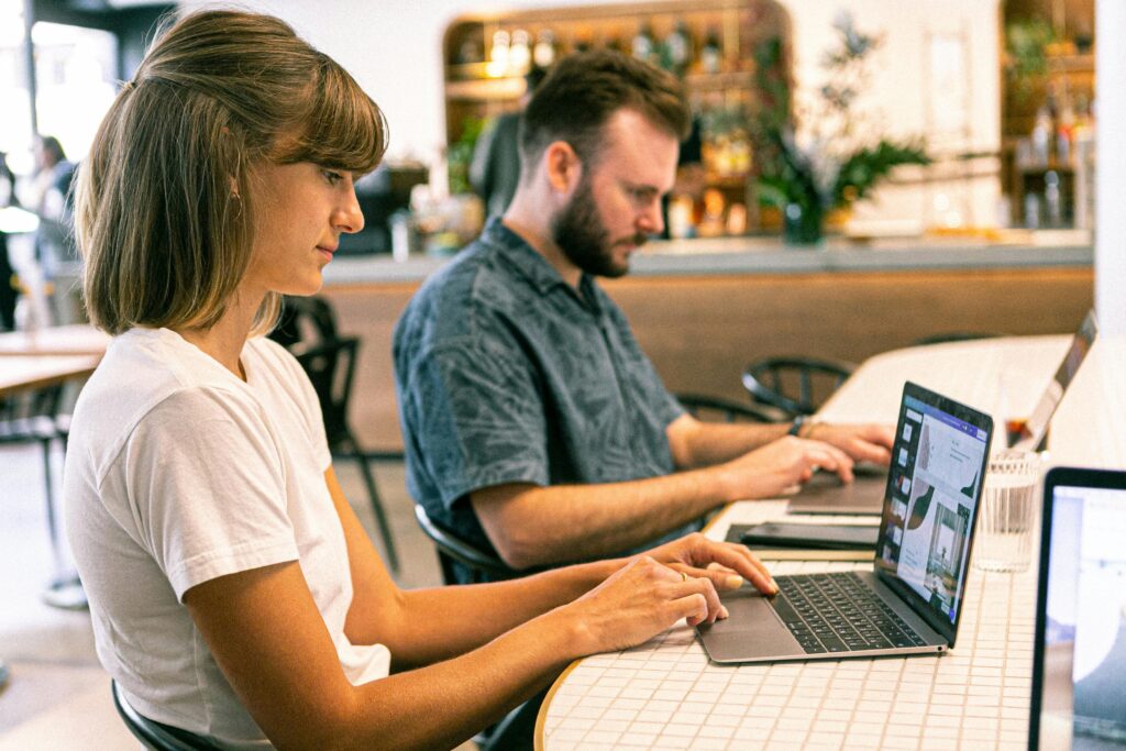 Two young professionals working on laptops in a modern cafe setting.Digital marketing service in kanhangad